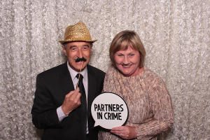 A couple in a FOTO Machines Photobooth holding a sign that says 'partners in crime'